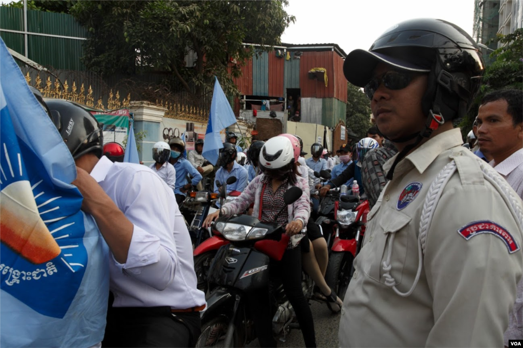 Á security police safeguards a self-claim university students group led by Srey Chamroeun. Some 70 students protest in front the house of CNRP's acting president Kem Sokha in Phnom Penh. Based on leaked phone records conversation, the group accused Kem Sokha of having immorally relations with a hairdresser Khom Chandarati. ( Leng Len/VOA Khmer) 