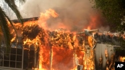 FILE - The Woolsey Fire burns a home in Malibu, Calif., Nov. 9, 2018. Flames forced total evacuation of the celebrity enclave.