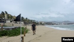 Un hombre camina cerca de una bandera negra, lo que significa que las condiciones del mar son extremadamente peligrosas, ante la llegada del huracán Kay, en Cabo San Lucas, en el estado de Baja California Sur, México, 6 de septiembre de 2022. REUTERS/Monserrat 