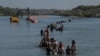 Una caravana pasa junto a una serie de boyas, que se construyen para disuadir a los migrantes de cruzar el río Grande, mientras buscan una abertura en el alambre de concertina para ingresar a Eagle Pass, Texas, EEUU, el 27 de julio de 2023.