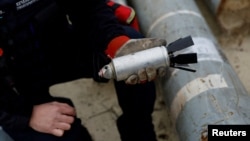 FILE - A member of the Ukrainian military holds a defused cluster bomb among a display of pieces of Russian army rockets that a Ukrainian munitions expert said did not explode on impact, in Kharkiv region, Ukraine, Oct. 21, 2022. 