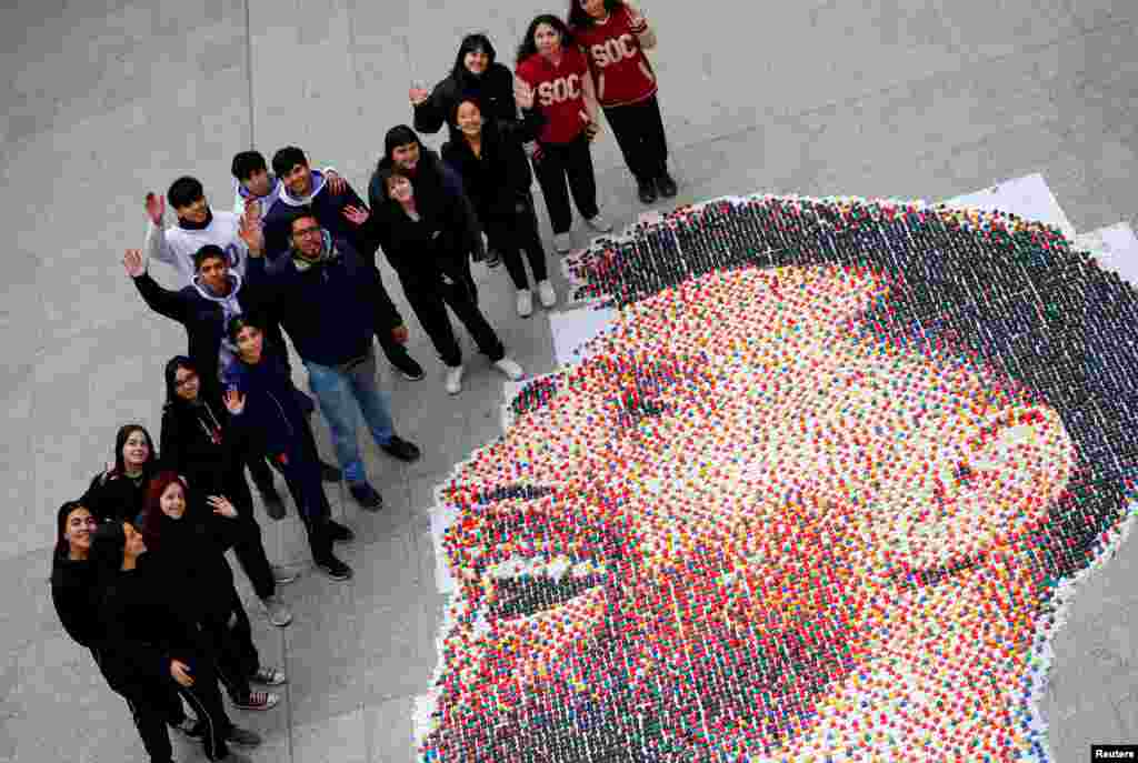 Art teacher Sebastian Ramirez waves with his students next to the mural they made with plastic bottle caps depicting Argentina's soccer superstar Lionel Messi, in Grand Bourg, on the outskirts of Buenos Aires.