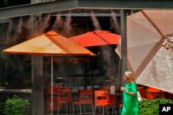 Una mujer camina bajo los chorros de agua afuera de un restaurante, el 12 de julio de 2023 en Gilbert, Arizona.