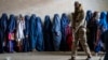 FILE - A Taliban fighter stands guard as women wait to receive food rations distributed by a humanitarian aid group, in Kabul, Afghanistan, May 23, 2023. 