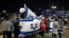 People hold flags of Israel and cheer after a vehicle carrying hostages released by Hamas passed towards an army base in Ofakim, southern Israel, on Nov. 26, 2023, after hostages were released by Hamas from the Gaza Strip.