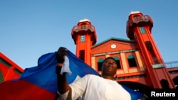 Una mujer haitiana que sostiene la bandera nacional del país en su espalda asiste a la inauguración del reconstruido mercado de hierro Hyppolite en Puerto Príncipe, el 11 de enero de 2011.