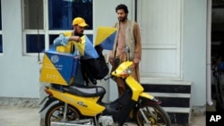 A postman delivers to a man in front of his house in the city of Kabul, Afghanistan, July 3, 2024.