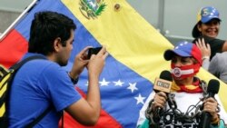 ARCHIVO - Un hombre toma una fotografía de una mujer que, mientras sostiene micrófonos, lleva una mordaza y una cadena. Fue durante una manifestación para conmemorar el día Mundial de la Libertad de Prensa en Caracas, Venezuela, el 3 de mayo de 2016.