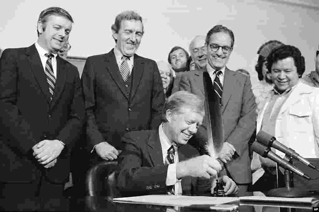 President Jimmy Carter uses an Indian quill pen to sign H.R.7919 the Maine Indian Claims Settlement Act of 1980 at a ceremony at the White House, Oct. 10, 1980.