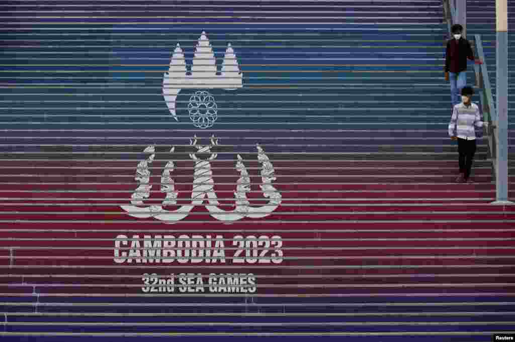 អ្នកទស្សនាពីរនាក់ដើរកាត់បដានៃការប្រកួតកីឡាស៊ីហ្គេមលើកទី ៣២ នៅពហុកីឡដ្ឋានជាតិមរតកតេជោ ក្នុងរាជធានីភ្នំពេញ កាលពីថ្ងៃទី ២ ខែឧសភា ឆ្នាំ ២០២៣។ 