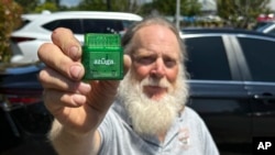 Evan Burroughs, who touts the virtues of an Oregon pilot program that charges motorists by the distance their vehicle travels rather than the gas it uses, displays a tracking device the program uses, in Salem, Ore., June 21, 2023. 