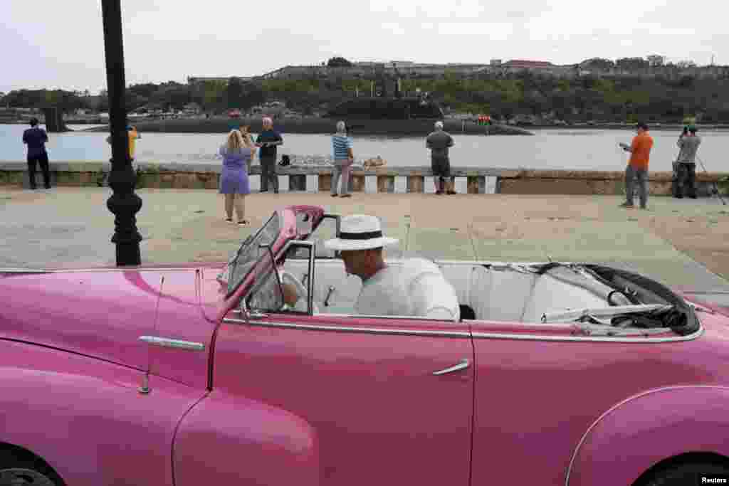 A driver parks a vintage car as Russian nuclear-powered cruise missile submarine Kazan enters Havana’s bay, Cuba.