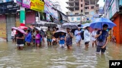 People carrying umbrellas, wade through a flooded street amid rainfall in Feni, Bangladesh, on Aug. 22, 2024.