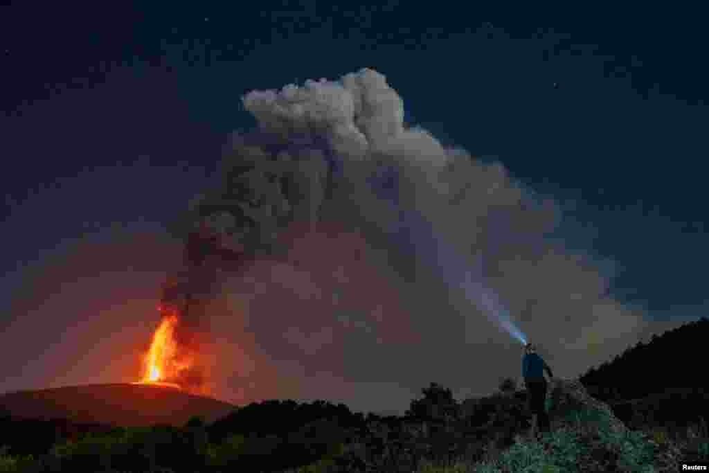 A person looks on as lava and plumes of smoke rise from a crater of Mount Etna, Europe's most active volcano, Italy, July 15, 2024.