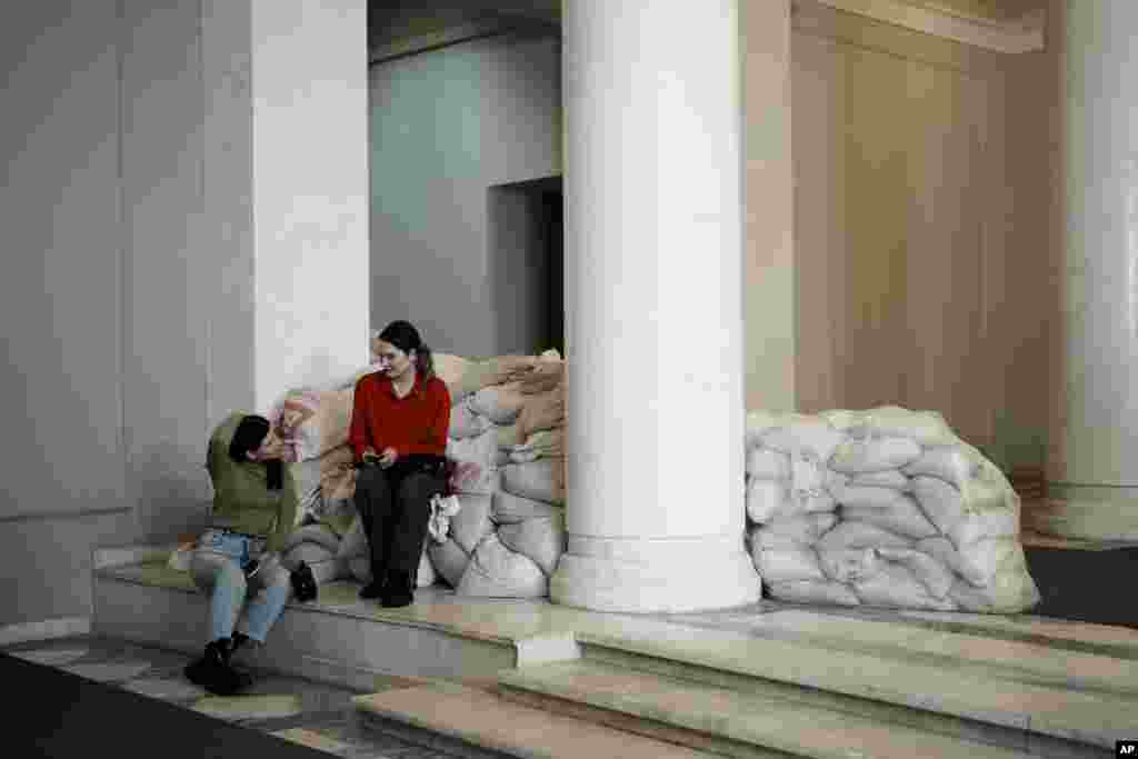 Dos reporteras, sentadas sobre sacos de arena en el interior de un edificio en Kiev, Ucrania, el 27 de febrero de 2023. Hay sacos de arena protegiendo estatuas y barreras antitanque en las calles, trincheras en los bosques cercanos y avisos de minas terrestres en el monte. Las señales pintadas en las paredes indican el refugio más próximo, mientras las sirenas antiaéreas suenan ocasionalmente en la ciudad, que a veces sufre ataques con misiles. 