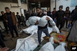A Palestinian man carries the body of his relative killed in the Israeli bombardment of the Gaza Strip, outside a morgue in Rafah, southern Gaza, Dec. 29, 2023.