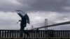 Un peatón lleva un paraguas mientras camina frente al puente de la bahía de San Francisco-Oakland en San Francisco, el martes 21 de marzo de 2023. (Foto AP/Jeff Chiu)