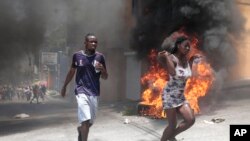 Demonstrators run past tires set on fire during a protest against insecurity in Port-au-Prince, Haiti, Aug. 7, 2023. 