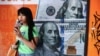 Una mujer bebe jugo junto a una casa de cambio con billetes de dólares estadounidenses impresos en sus ventanas en Buenos Aires, Argentina, 12 de diciembre de 2023. 