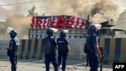 Aparat kepolisian Bangladesh berdiri di samping truk kargo setelah dibakar oleh pekerja garmen di Shafipur, 31 Oktober 2023, sebagai bagian dari demontrasi menuntut kenaikan upah. (Foto: AFP)