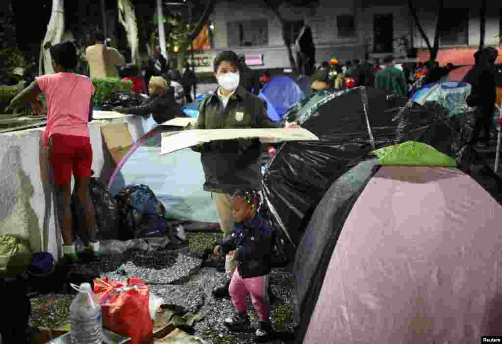 Una integrante del Instituto Nacional de Migración ayuda a los migrantes en el parque Giordano Bruno, a ser trasladados a un albergue.