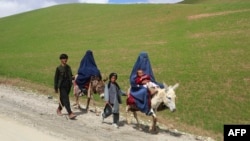 Mujeres afganas vestidas con burka montan en burro junto a niños en una carretera cerca de la aldea de Shah Mari en el distrito de Argo, provincia de Badakhshan, Afganistán, el 1 de mayo de 2024.