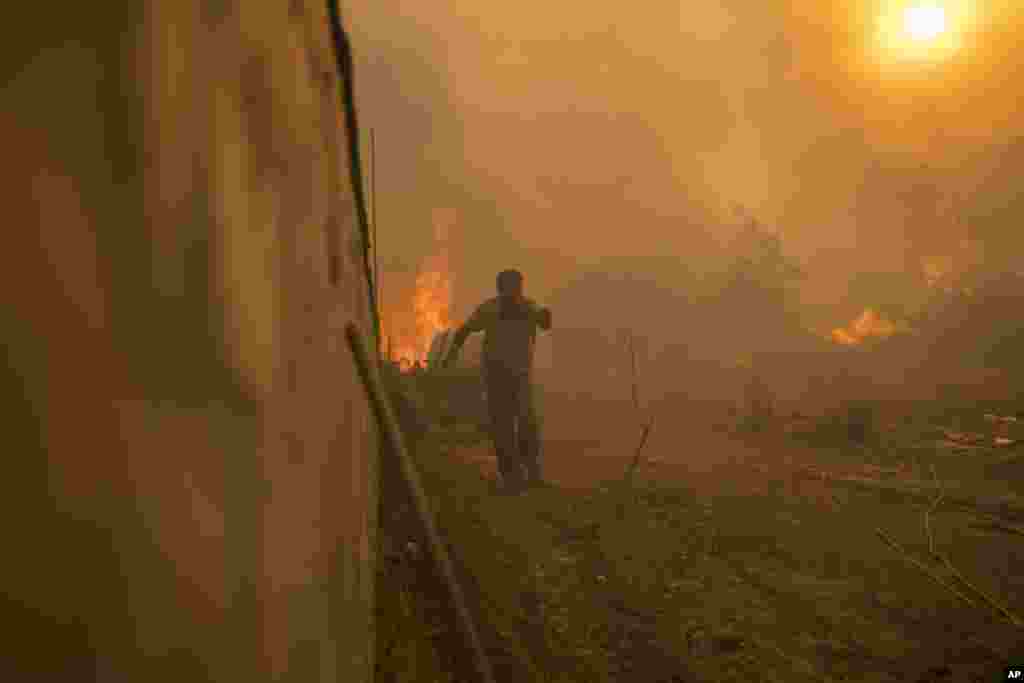 A local runs to avoid the flames of a wildfire in Gennadi village, on the Aegean Sea island of Rhodes, southeastern Greece, July 25, 2023. A firefighting plane has crashed in southern Greece, killing both crew members, as authorities are battling fires across the country amid a return of heat wave temperatures.