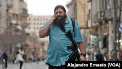 Una persona de paisano camina por una calle de Jerusalén con su fusil automático, una escena cotidiana en los vecindarios y calles de la legendaria Ciudad Santa. [Foto: Alejandro Ernesto, VOA]