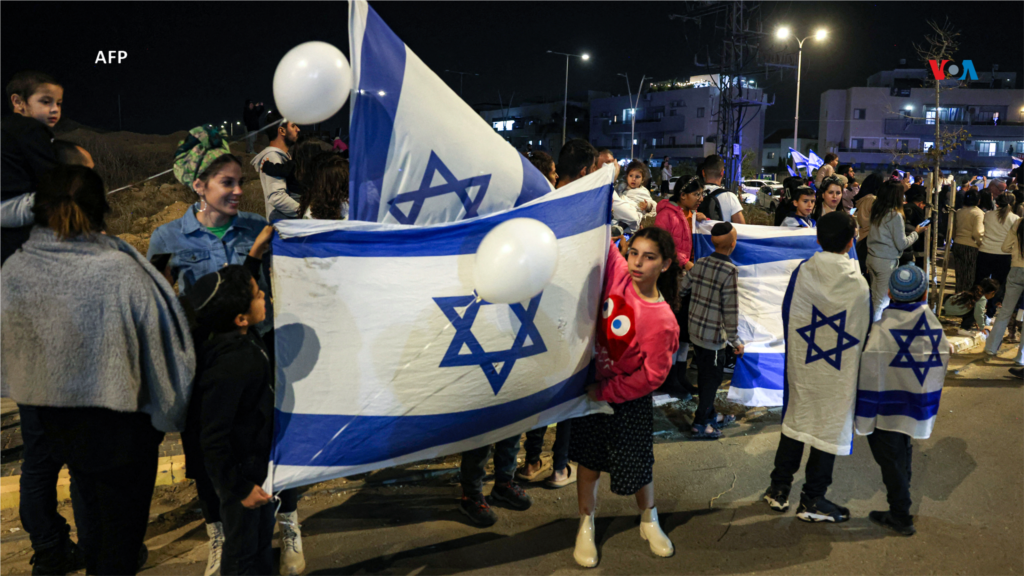 La gente sostiene banderas de Israel y aplaude después de que un vehículo que transportaba rehenes liberados por Hamás pasara hacia una base militar en Ofakim, en el sur de Israel.
