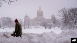 El edificio del Capitolio del Estado de Iowa es visible mientras Spud Glaser de Carlisle, Iowa, limpia la acera en el centro de Des Moines, Iowa, el martes 9 de enero de 2024, mientras una tormenta de nieve invernal azota el estado. (Foto AP/Andrew Harnik)