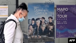 FILE - A woman walks past a poster featuring members of the K-pop group BTS, at a tourist information center in Seoul, South Korea, June 15, 2022.