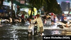 ស្រ្តី​ម្នាក់​កំពុង​បណ្តើរ​ម៉ូតូ​ដែល​ខូច​ដោយសារ​ទឹក​លិច​ ​លើ​បណ្តោយ​ផ្លូវ​ហ្សាល​ដឺហ្គោល រាជធានី​ភ្នំពេញ​ នៅ​ថ្ងៃទី២៣ ខែ​មិថុនា ឆ្នាំ​២០២២។ (កាន់ វិច្ឆិកា/វីអូអេ)