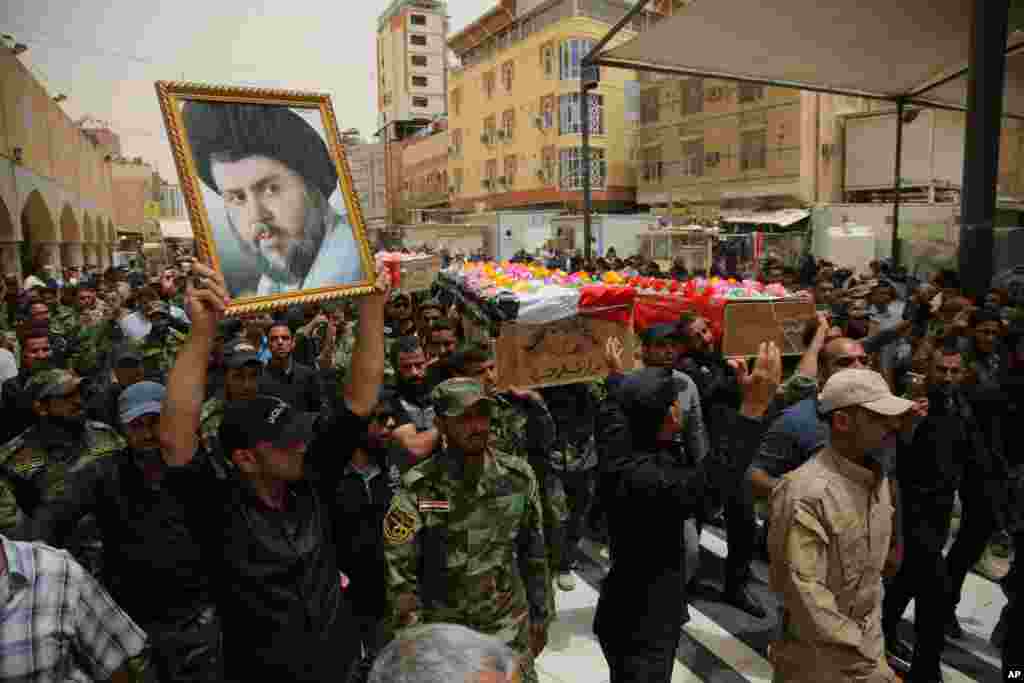 Mourners chant slogans against the Islamic State group as they carry the flag-draped coffins of three members of the Peace Brigades, a Shi'ite militia group loyal to Shi'ite cleric Muqtada al-Sadr, who were killed during fighting with Islamic State militants, during the funeral in Najaf, south of Baghdad, May 27, 2015.