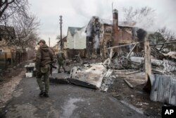 Ukrainian servicemen walk at fragments of a downed aircraft seen in in Kyiv, Ukraine, Friday, Feb. 25, 2022. It was unclear what aicraft crashed and what brought it down amid the Russian invasion in Ukraine Russia is pressing its invasion of Ukraine to the outskirts of the capital after unleashing airstrikes on cities and military bases and sending in troops and tanks from three sides. (AP Photo/Oleksandr Ratushniak)