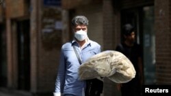 FILE: An Iranian man holds stacks of bread as he walks along a street in Tehran, Iran, May 1, 2022.