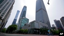 Una mujer con una mascarilla para protegerse del coronavirus pedalea en una calle tranquila junto al cerrado World Trade Center de China, izquierda, luego de que se detectara un caso de COVID-19 en el edificio el lunes 9 de mayo de 2022 en Beijing. (Foto 