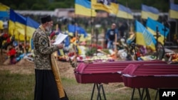 A chaplain leads a funeral service for Ukrainian servicemen Sergiy Profotilov and Igor Malenkov, both killed in the village of Vilkhivka during the Russian invasion of Ukraine, in the military section of Kharkiv cemetery number 18 in Bezlioudivka, eastern Ukraine, May 21, 2022.