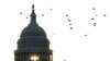 La silueta de un peatón temprano en la mañana contra el amanecer mientras camina frente a las banderas de EEUU en el National Mall y pasa por el edificio del Capitolio en Washington, el 7 de noviembre de 2022.