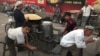 FILE - Uighurs rest near a food stall and Beijing Olympic Games billboards in Kashgar in China's western Xinjiang province, Aug. 30, 2016.