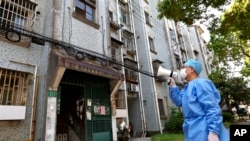 Seorang relawan menggunakan megafon ketika berbicara dengan para warga di sebuah komplek apartemen di Shanghai, China, di tengah lockdown yang diberlakukan di wilayah tersebut, pada 12 April 2022. (Foto: Xinhua via AP/Chen Jianli)