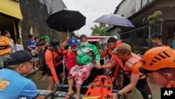 In this handout photo provided by the Philippine Coast Guard, rescuers evacuate a resident to safer ground at Abuyog, Leyte province, central Philippines on Sunday April 10, 2022. (Philippine Coast Guard via AP)