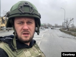 El reportero de investigación ucraniano Denis Kazansky muestra a sus espaldas autos civiles destruidos en la ciudad de Bucha, cerca de Kiev, 4 de abril de 2022. [Cortesía de Denis Kazansky]
