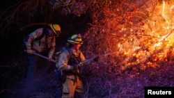 Firefighters extinguish the fire as the Palisades Fire, one of several simultaneous blazes that have ripped across Los Angeles County, burns in Mandeville Canyon, a neighborhood of Los Angeles, California, Jan. 12, 2025.
