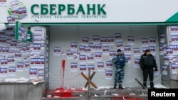 FILE - Security staff stand guard after a protest held by members of the Azov civil corps outside the central branch of Sberbank in Kyiv, Ukraine, Feb. 2, 2017. The stickers read "Attention. This is a bank of the aggressor state. It will be closed. Immediately take back your money."