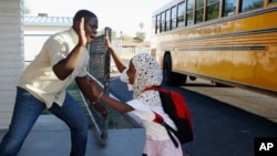 Samuel Lavi, left, a Congolese native who is a teaching assistant and family engagement liaison, greets first grader Kediga Ahmed as she arrives at the Valencia Newcomer School attend class, Oct. 17, 2019, in Phoenix. (AP Photo/Ross D. Franklin)