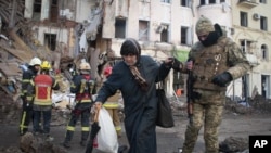 Un voluntario de las Fuerzas de Defensa Territorial de Ucrania ayuda a una mujer a cruzar la calle en Kharkiv, Ucrania, el miércoles 16 de marzo de 2022.