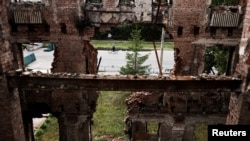 FILE -- A man rides his bicycle in front of a school destroyed in a military attack, as Russia's invasion of Ukraine continues, in Kharkiv, Ukraine, July 14, 2022.