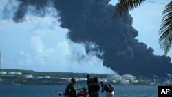 La gente observa una enorme columna de humo que se eleva desde la base de supertanqueros de Matanzas, mientras los bomberos intentan sofocar un incendio que comenzó durante una tormenta eléctrica la noche anterior, en Matazanas, Cuba, el sábado 6 de agosto de 2022. (Foto AP/Ramón Espinosa)