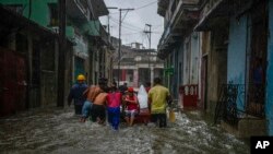 Voluntarios empujan a una mujer en un bote por una calle de un barrio inundada por fuertes lluvias, en La Habana, Cuba, el viernes 3 de junio de 2022. (AP Foto/Ramon Espinosa)