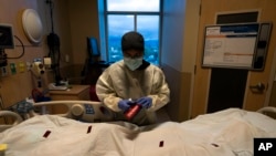 FILE - Registered nurse Bryan Hofilena attaches a "COVID Patient" sticker on a body bag of a patient who died of coronavirus at Providence Holy Cross Medical Center in Los Angeles.